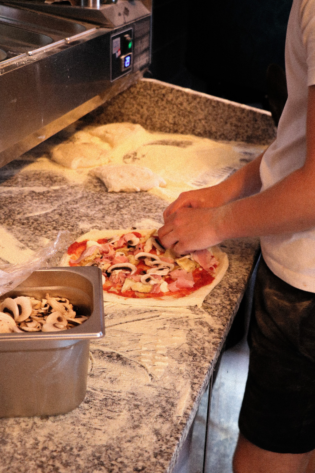 Le pizzaiolo garnit une Cappriciosa : jambon, champignons, artichauts