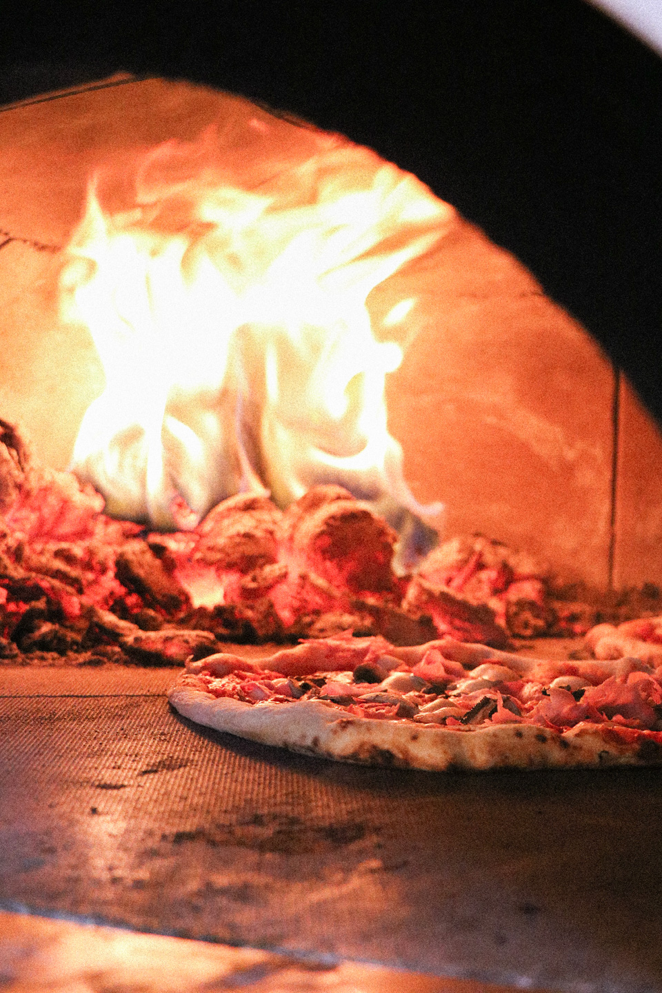 Une pizza en cuisson devant les flammes du four à bois